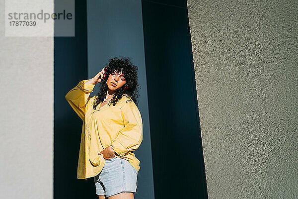 Frau mit der Hand im Haar an der Wand an einem sonnigen Tag