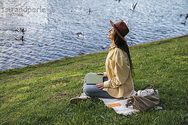 Lächelnde Frau sitzt mit Laptop im Park