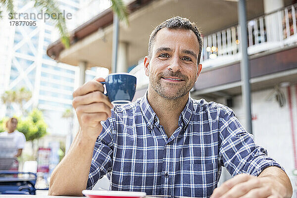 Lächelnder Mann mit einer Tasse Kaffee sitzt im Straßencafé