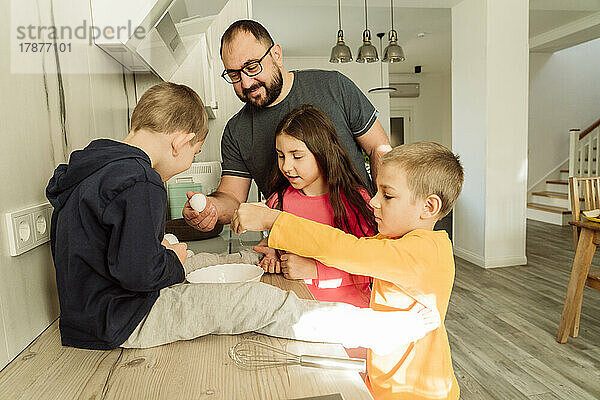 Lächelnder Mann mit Kindern bereitet Frühstück in der Küche zu