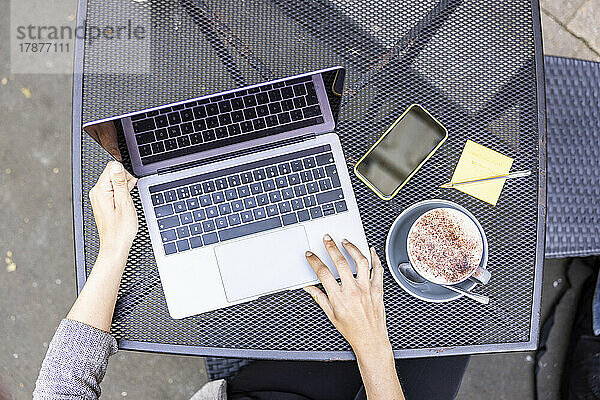 Hände einer Geschäftsfrau mit Laptop am Tisch eines Straßencafés