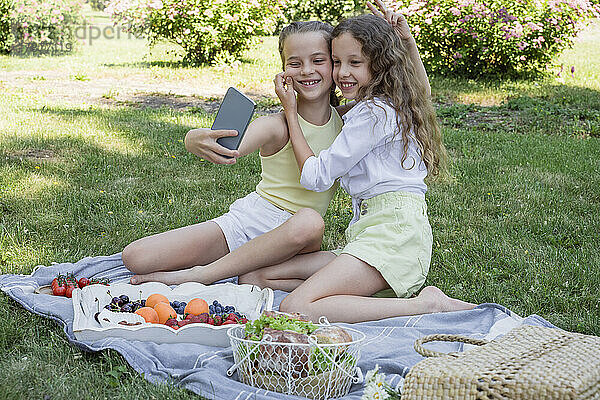 Mädchen zieht die Wange ihrer Schwester und macht ein Selfie im Park