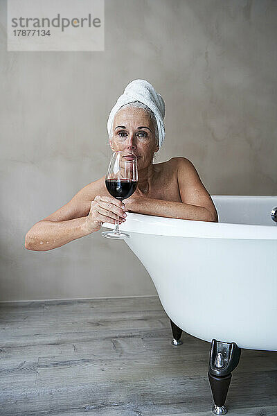 Mature woman having red wine in bathroom