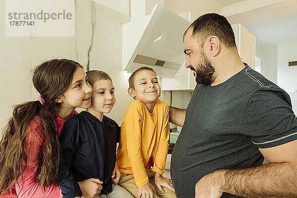 Lächelnder Vater spricht mit Kindern in der Küche