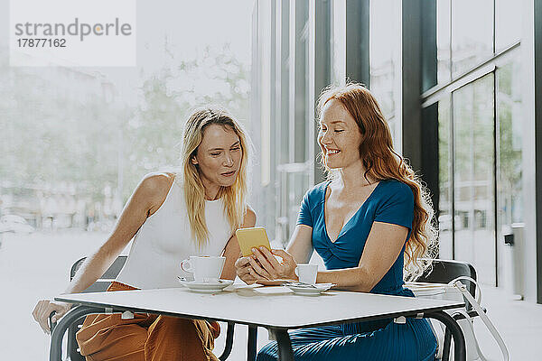Frau teilt Mobiltelefon mit Freundin im Café