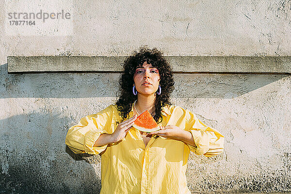 Frau mit Wassermelonenscheibe vor der Wand