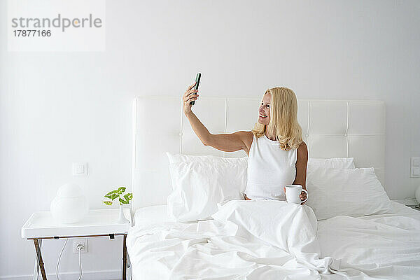 Frau macht Selfie mit Handy und sitzt im Bett