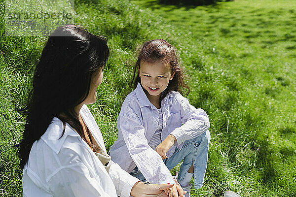 Lächelndes Mädchen  das an einem sonnigen Tag mit seiner Mutter auf der Wiese spricht