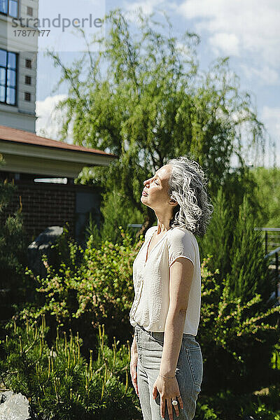 Frau steht mit geschlossenen Augen und genießt das Sonnenlicht im Park