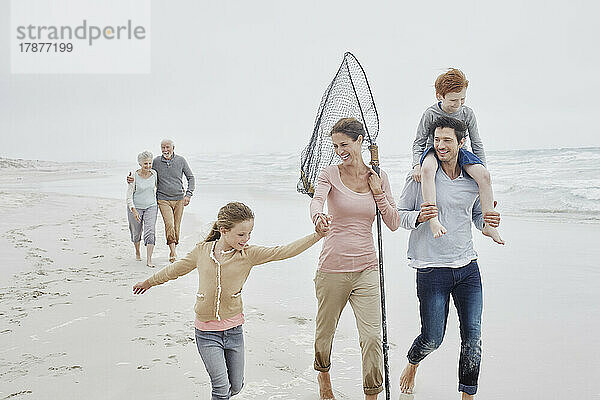 Sorglose Familie mit Tochter  die am Strand spaziert  die Großeltern folgen im Hintergrund