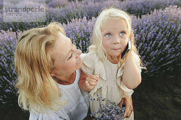 Glückliche Frau mit süßer Tochter  die im Lavendelfeld auf dem Smartphone spricht