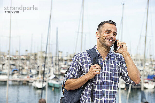 Lächelnder reifer Mann  der am Hafen mit dem Smartphone spricht