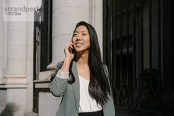 Junge Frau telefoniert vor dem Gebäude mit dem Smartphone