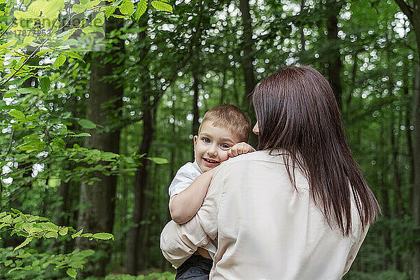 Mutter trägt lächelnden Sohn im Wald