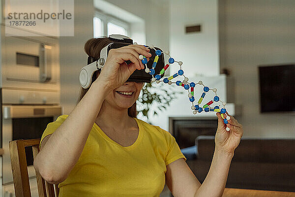 Lächelnde Frau mit VR-Brille und DNA-Modell zu Hause