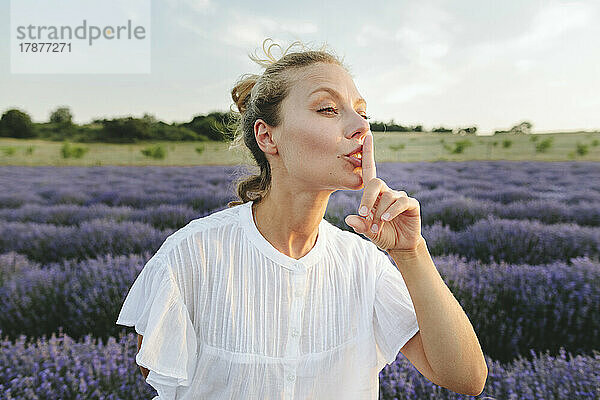 Frau gestikuliert mit dem Finger auf den Lippen und steht im Lavendelfeld