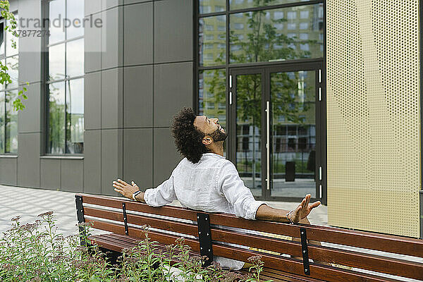 Glücklicher Mann  der auf einer Bank in der Nähe des Gebäudes sitzt und nach oben schaut