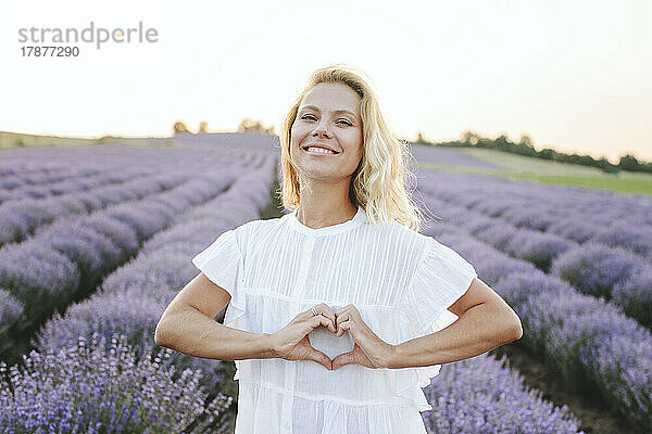 Glückliche Frau gestikuliert Herzform im Lavendelfeld