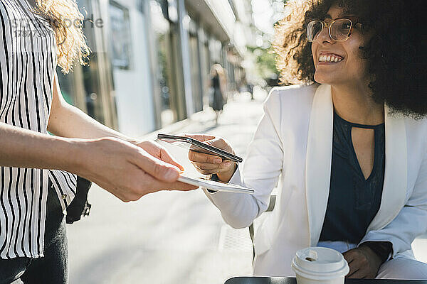 Junge Geschäftsfrau bezahlt per Smartphone im Straßencafé