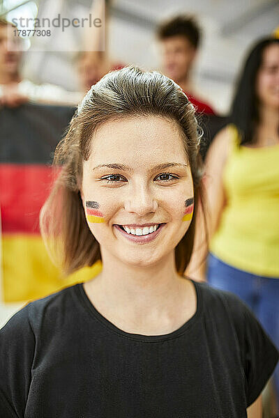 Lächelnde Frau mit aufgemalter deutscher Flagge im Gesicht bei Sportveranstaltung im Stadion