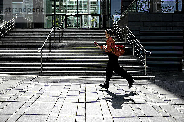 Geschäftsfrau läuft mit Mobiltelefon auf Fußweg