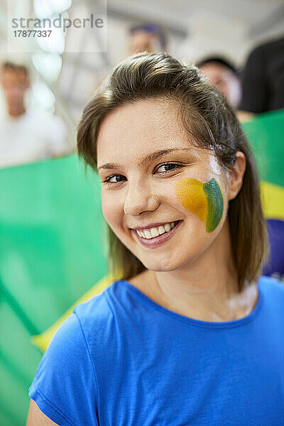 Junge lächelnde Frau zeigt Brasilien-Flagge im Gesicht