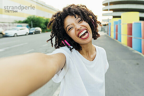 Fröhliche junge Frau mit lockigem Haar macht ein Selfie
