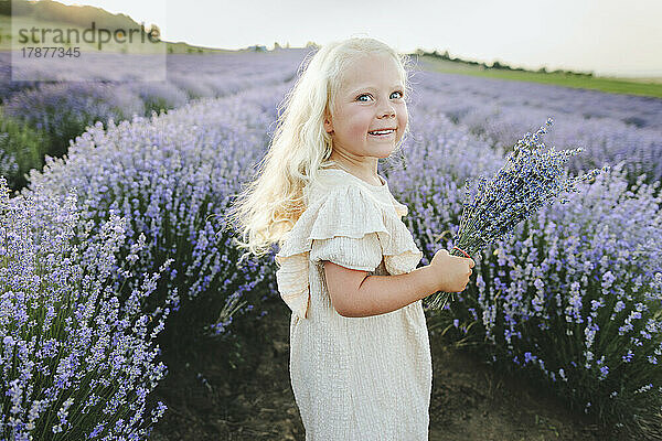 Happy girl with bunch of lavender flowers standing in field