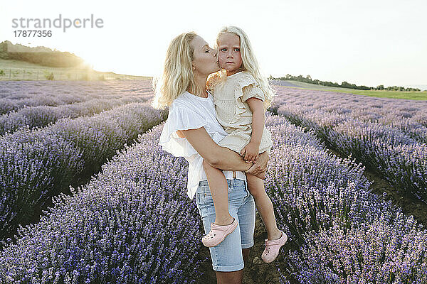 Mother kissing daughter in lavender field at sunset
