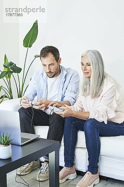 Mother and son playing video game on laptop at home