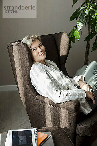 Lächelnde reife Frau entspannt sich zu Hause im Sessel