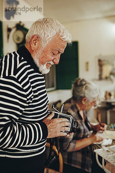 Älterer Mann untersucht Kamera von Frau  die zu Hause malt