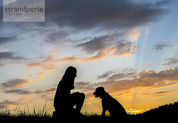 Silhouette einer Frau  die bei Sonnenuntergang mit Hund gegen Wolken spielt