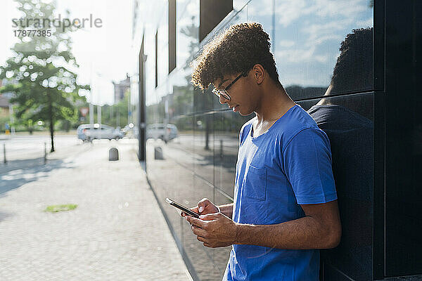 Junger Mann benutzt Mobiltelefon und lehnt an Wand