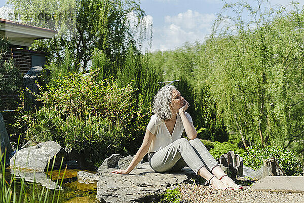 Lächelnde Frau sitzt an einem sonnigen Tag im Park