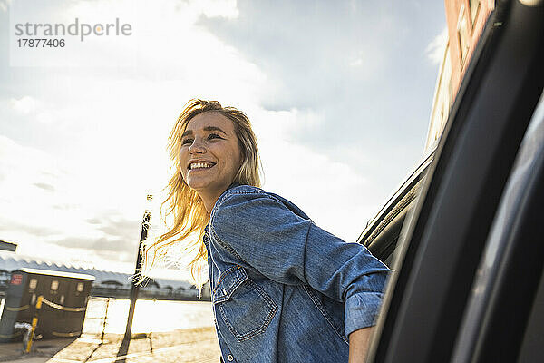 Smiling young woman leaning out of car window at sunset