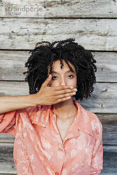 Junge Frau bedeckt den Mund mit der Hand vor einer Holzwand