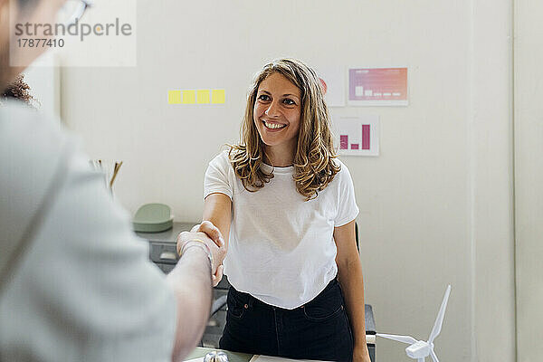 Lächelnde Geschäftsfrau schüttelt einem Kollegen im Büro die Hand