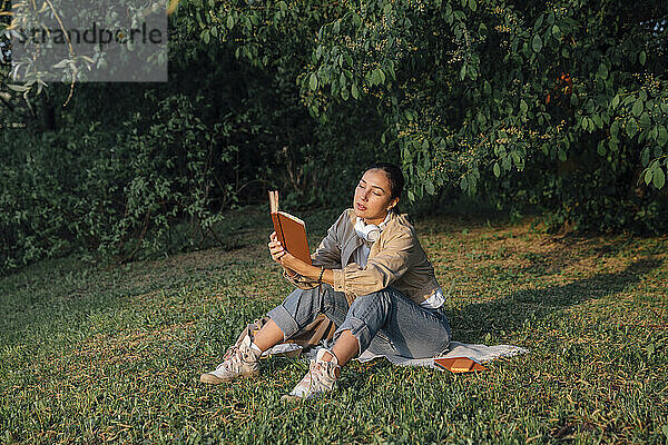 Frau liest Buch und sitzt auf Gras im Park