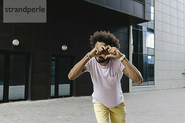 Man making heart gesture in front of building