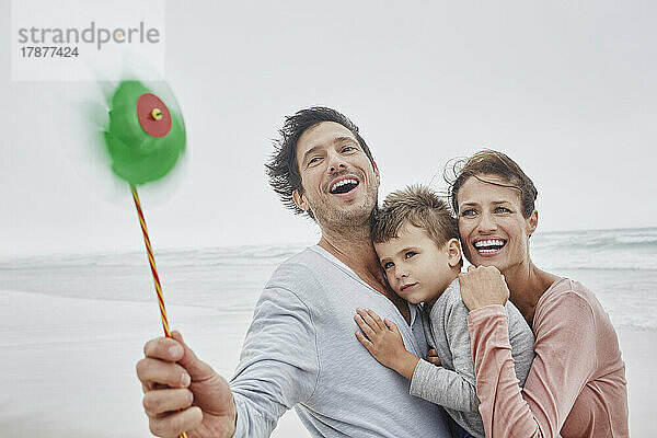 Glückliche Familie steht am windigen Strand und hält ein grünes Oinwheel in der Hand