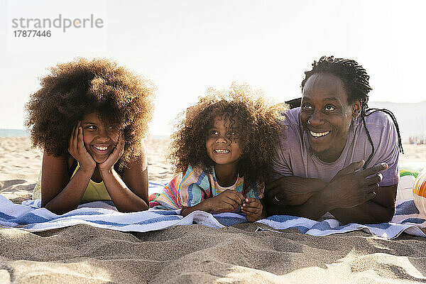 Lächelnde Töchter und Vater liegen zusammen am Strand