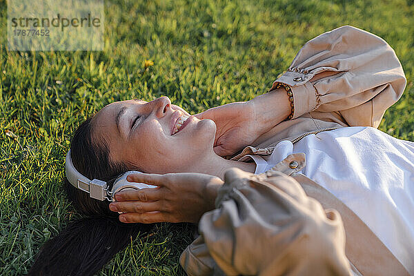 Lächelnde Frau  die im Park Musik über kabellose Kopfhörer hört