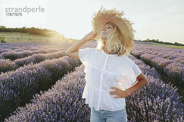 Lächelnde Frau mit Hut genießt das Lavendelfeld