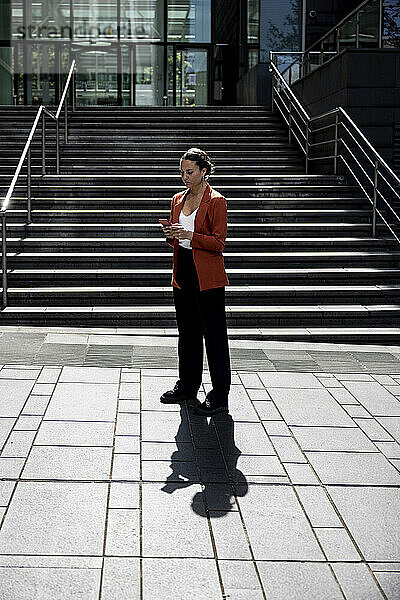 Geschäftsfrau benutzt Smartphone auf Fußweg vor Treppe