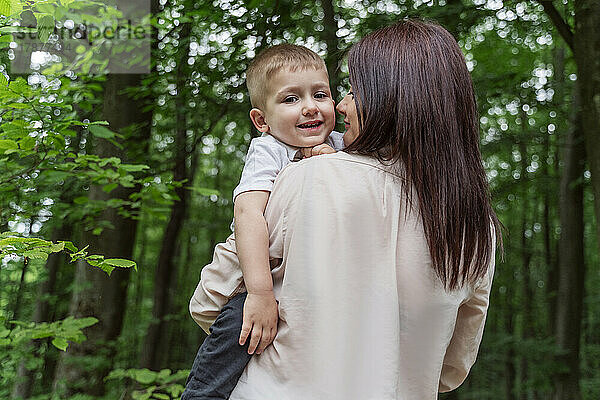 Happy son with mother amidst trees in forest