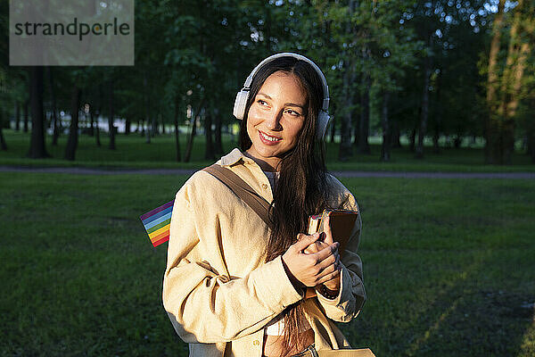 Lächelnde Frau mit Kopfhörern und Büchern im Park
