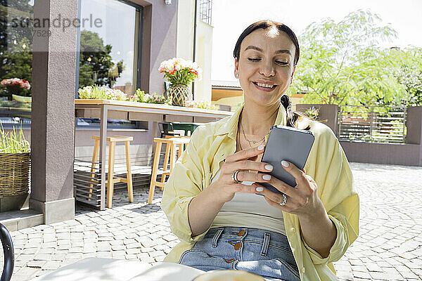 Lächelnde Frau benutzt Smartphone im Straßencafé