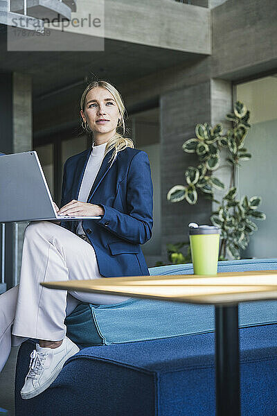 Nachdenkliche Geschäftsfrau mit Laptop sitzt auf der Couch im Büro