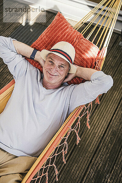 Happy man with hands behind head resting in hammock
